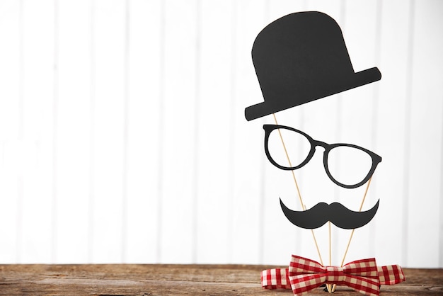 Noeud papillon avec chapeau à moustache en papier et lunettes sur table en bois