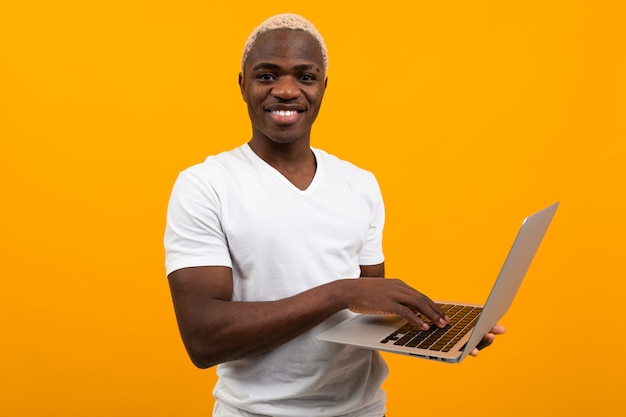 Noir américain avec un beau sourire blanc comme neige dans un T-shirt blanc avec un ordinateur portable sur fond orange