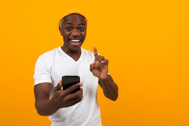 Noir américain homme souriant tenant un téléphone dans ses mains sur un fond orange