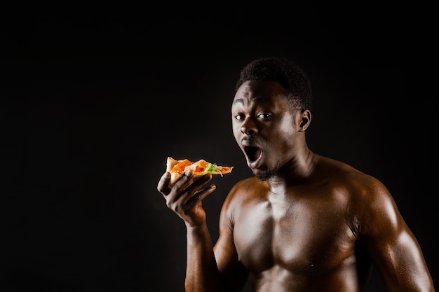 Noir bel homme nu mange une pizza