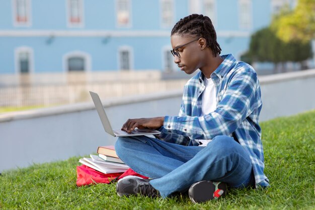 Un Noir concentré s'engage dans l'apprentissage électronique sur son ordinateur portable en plein air