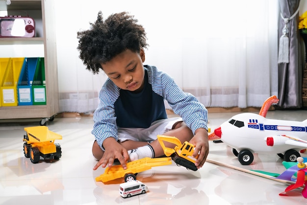 Des noirs heureux Un enfant afro-américain joue un camion et un jouet d'avion à la maison