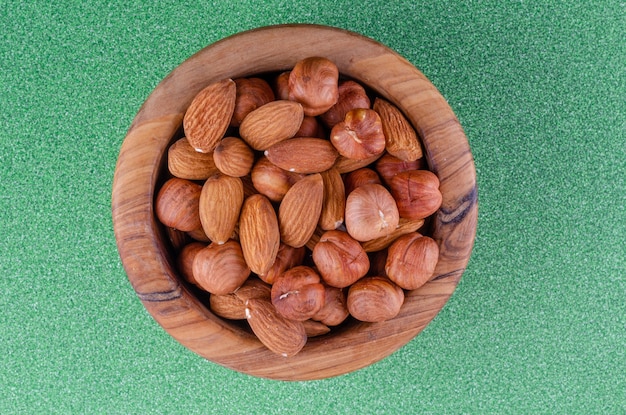 Photo noix en assortiment dans une assiette en bois sur fond vert.