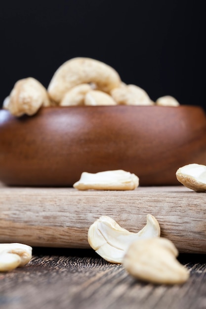 Noix de cajou sur une vieille table en bois et dans un bol en bois, gros plan d'un grand nombre de noix de cajou sur une table et sur une surface en bois dans une assiette en bois