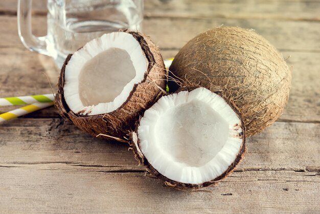 Noix de coco et bocal en verre avec de l'eau de coco vieux fond en bois aux tons de paille