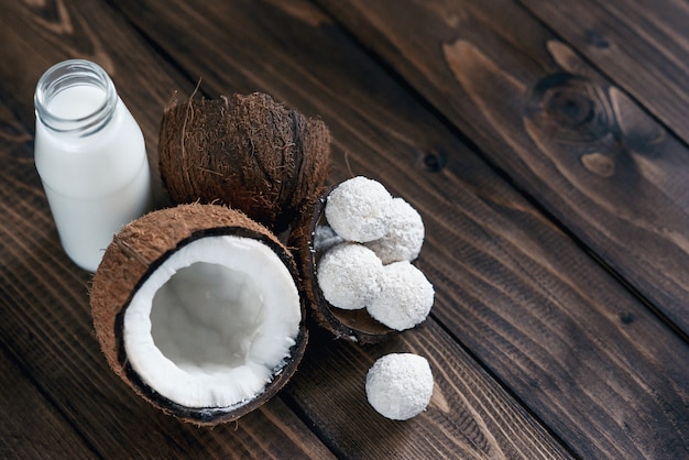 Noix de coco avec des bonbons en flocons de noix de coco et une bouteille de lait sur une table en bois.