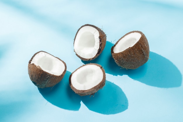 Noix de coco cassée sur une surface bleue sous la lumière naturelle avec des ombres. Lumière forte. Concept de régime alimentaire, alimentation saine, repos sous les tropiques, vacances et voyages, vitamines.