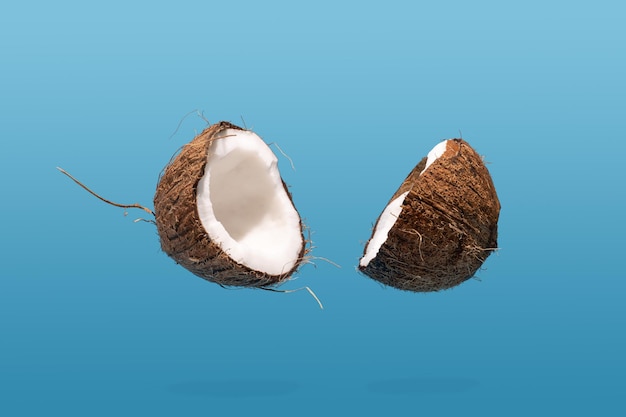 Noix de coco flottante divisée en deux sur fond bleu concept alimentaire créatif