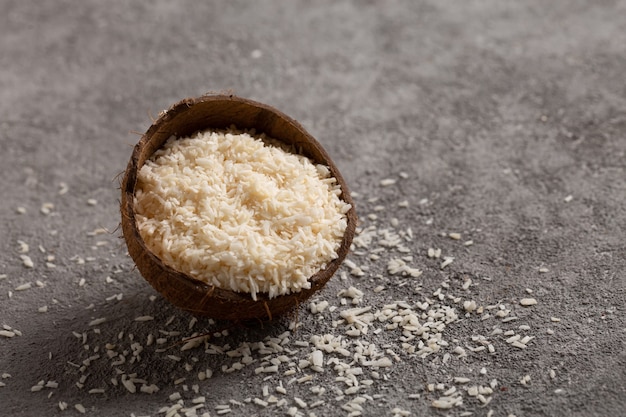 Noix de coco hachée avec des flocons de noix de coco sur fond de béton gris.