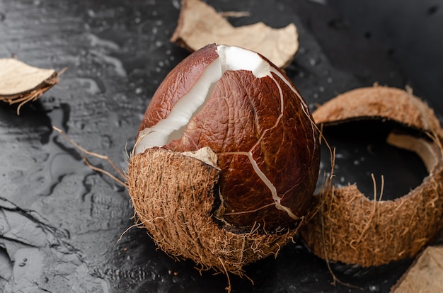 Noix de coco mûre brisée sur pierre d'ardoise noire