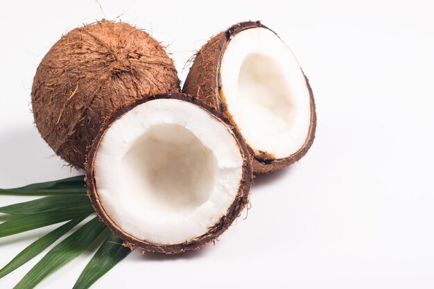 Noix de coco mûre à moitié coupée avec des feuilles vertes sur fond blanc