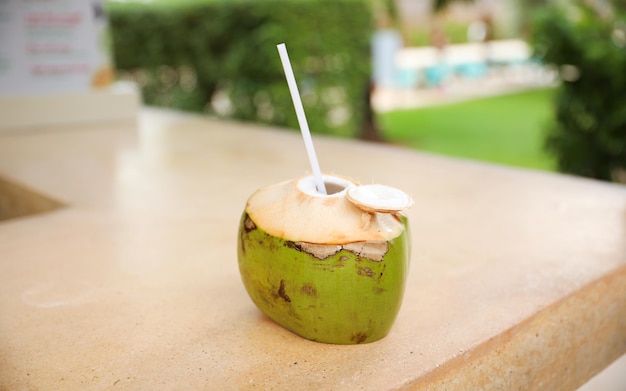 Une noix de coco avec une paille est placée sur une table à l'extérieur.