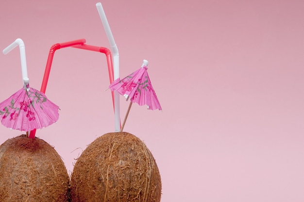 Noix de coco avec paille et parapluie sur fond rose