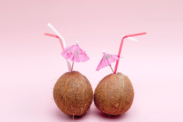 Noix de coco avec paille et parapluie sur fond rose