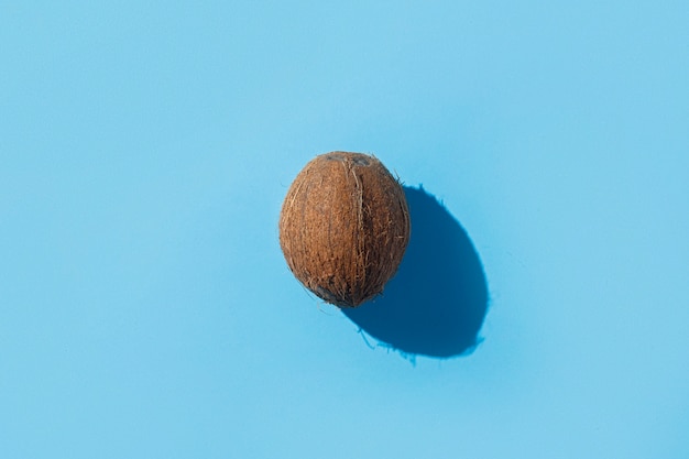 Noix de coco sur une surface bleue. Lumière forte. Concept des tropiques, alimentation saine, petit déjeuner, alimentation, vacances. Mise à plat, vue de dessus.