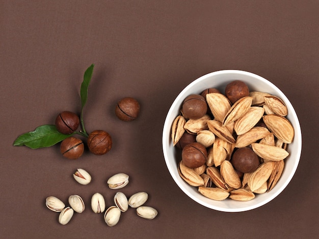 Noix crues dans un bol en bois macadamia et pistache sur fond de daim marron