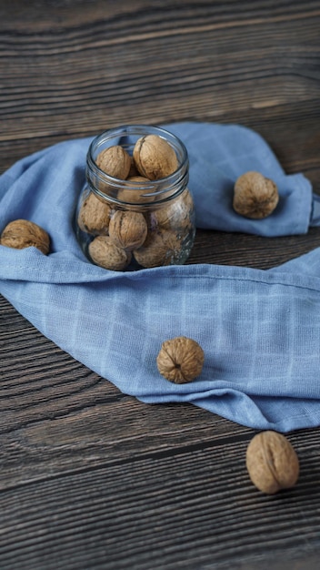 Noix dans un bocal en verre transparent sur un fond en bois, les textiles de cuisine bleus se trouvent à proximité