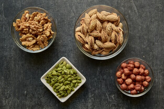 Noix dans des bols en verre et graines de citrouille pelées sur surface grise