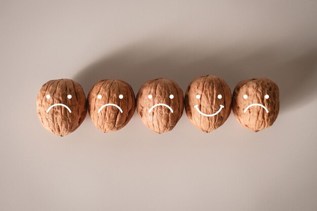 Des noix écorchées avec des visages stylisés de visages souriants et grincheux sur elles Être heureux et triste Concept d'expérience client