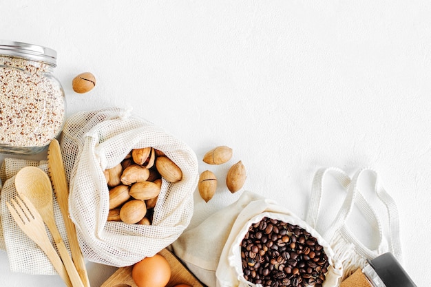 Noix, fruits secs et gruau dans des sacs en coton écologique et des bocaux en verre sur une table blanche dans la cuisine. Achats alimentaires zéro déchet. Vivre sans déchets