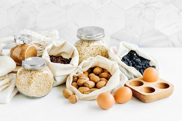 Noix, fruits secs et gruau dans des sacs en coton écologique et des bocaux en verre sur une table blanche dans la cuisine. Achats alimentaires zéro déchet. Vivre sans déchets