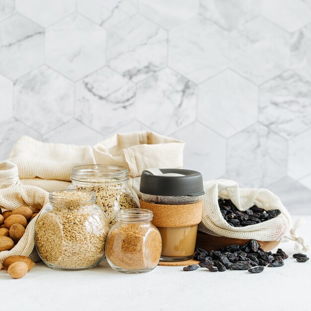 Noix, fruits secs et gruau dans des sacs en coton écologique et des bocaux en verre sur une table blanche dans la cuisine. Achats alimentaires zéro déchet. Vivre sans déchets