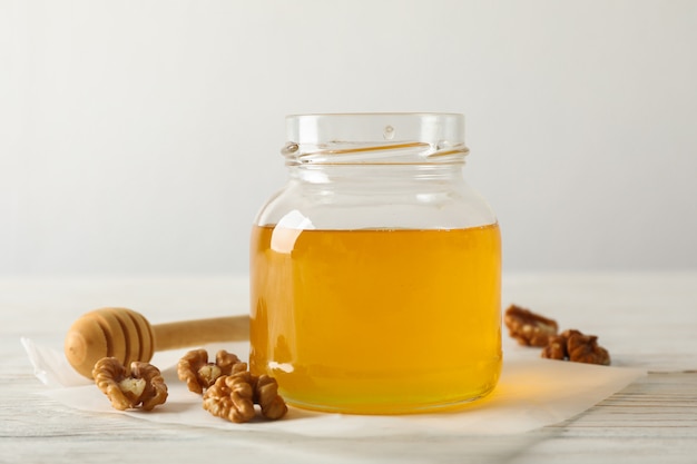 Noix, louche, parchemin et pot en verre avec du miel sur fond blanc