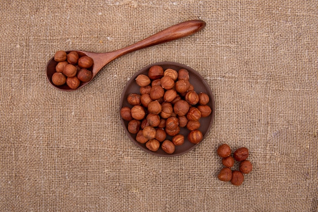 Noix de noisette dans une cuillère en bois et une assiette en faïence brune sur la vieille toile de jute