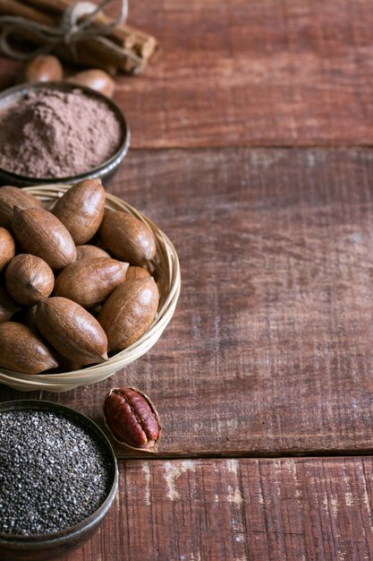 Noix de pécan, graines de chia et cacao dans des bols sur une table en bois