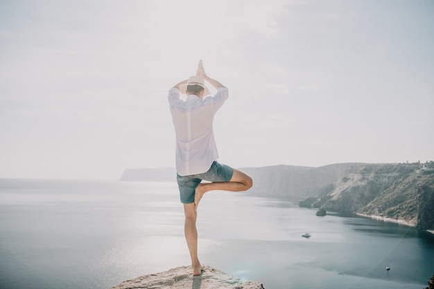 Un nomade numérique un homme au chapeau un homme d'affaires fait du yoga sur les rochers au bord de la mer au coucher du soleil fait un