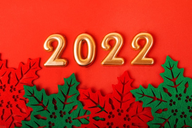 Nombres d'or 2022 sur fond rouge. Belles feuilles de houx décoratives en dessous. Fond de nouvel an.