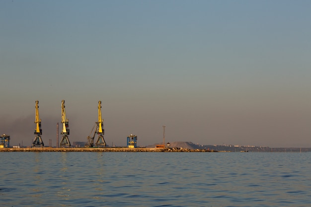 De nombreuses grosses grues se dessinent dans le port à la lumière dorée du coucher du soleil. Mariupol, Ukraine