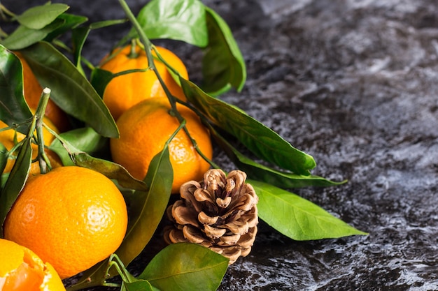 De nombreuses mandarines orange avec des feuilles vertes sur fond sombre avec espace de copie. Tranches et cônes de mandarines pelées