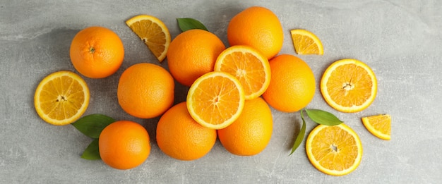 De nombreuses oranges mûres avec des feuilles sur une table grise, vue de dessus