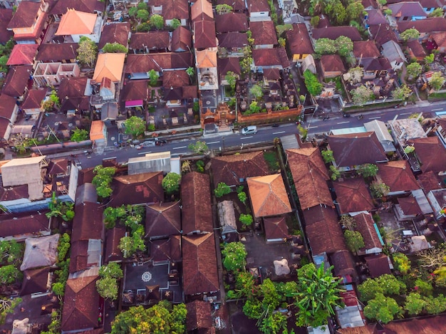 De nombreuses villas aux toits de bardeaux marron orange entre les arbres tropicaux sur fond de ciel à Ubud à Bali Le soleil brille sur eux Photo horizontale aérienne