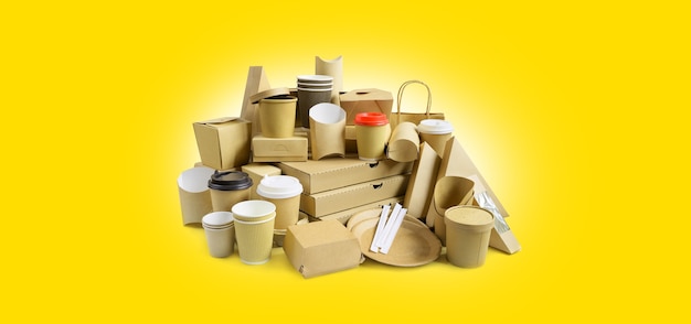 De nombreux contenants de plats à emporter différents, une boîte à pizza, des tasses à café dans un support et des boîtes en papier sur fond jaune.