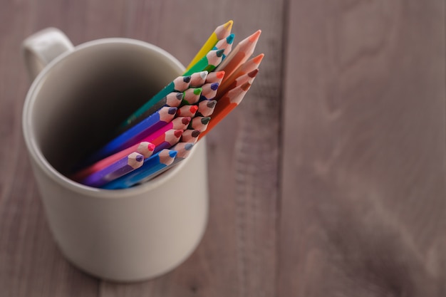 De nombreux crayons dans une tasse sur une table en bois