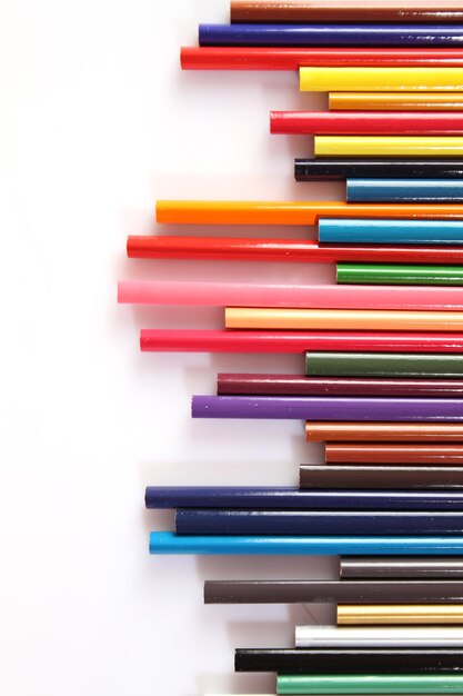 De nombreux crayons multicolores se trouvent dans une rangée sur un fond blanc