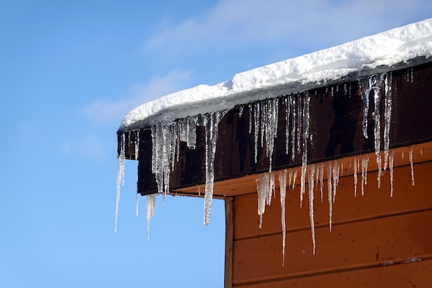 Photo de nombreux glaçons en fusion avec des gouttes tombées pendent de près sur le bord du toit