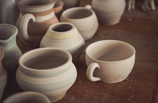 De nombreux pots en argile sont sur la table en poterie. Poterie lumineuse. Beaucoup de poterie en argile blanche non peinte, debout sur une table en bois. Potier de studio créatif. Assistant de lieu de travail Crock poterie