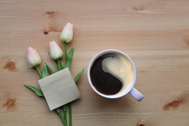 Note collante de tasse de café et tulipes roses sur la table en bois