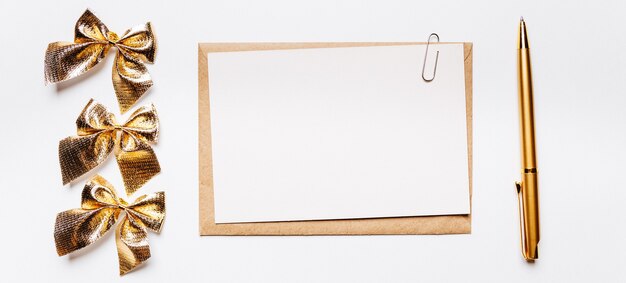 Note vierge avec enveloppe, arc et stylo or sur fond blanc