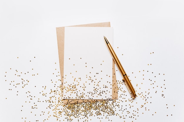 Note vierge avec enveloppe, stylo et étoiles de paillettes d'or sur fond blanc