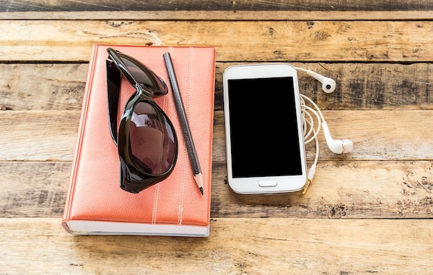 Notebooksunglassessmart phone et écouteurs sur table en bois