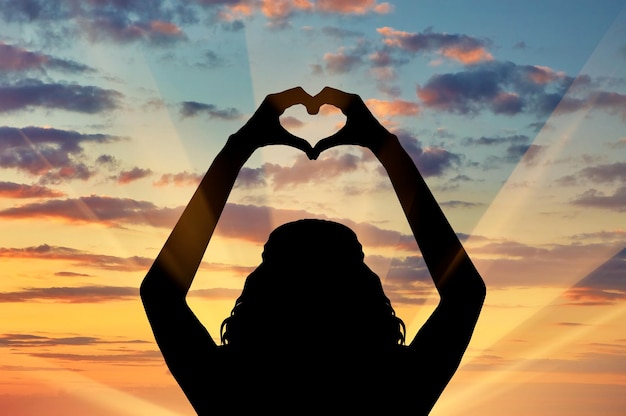 Photo notion d'amour. silhouette d'une fille montrant son amour de symbole de coeur de mains au coucher du soleil