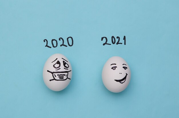 Notion de covid-19. Oeufs aux visages dessinés à la main sur fond bleu. 2020 vs 2021