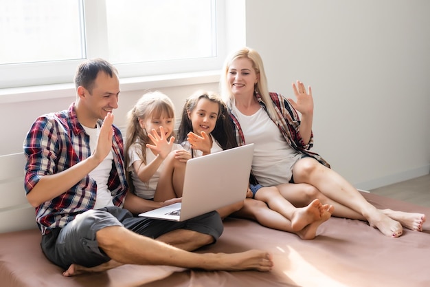 Notion de famille heureuse. Belle mère et beau père avec leurs filles qui passent du temps ensemble à la maison et allongées sur le lit avec un ordinateur portable.