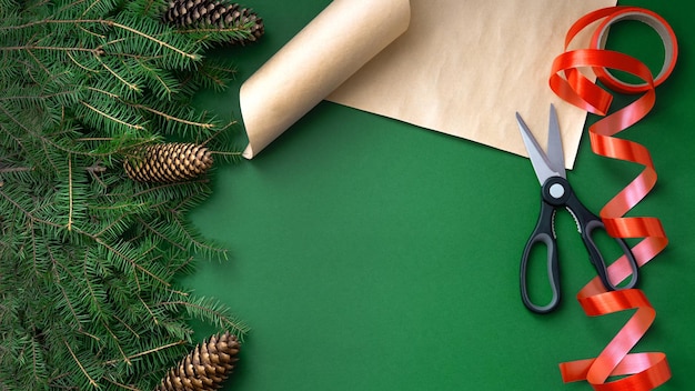 Notion de fond de Noël. Vue de dessus sur fond vert, avec des branches de sapin, des cônes, un ruban rouge et des ciseaux sur papier. Emballez les cadeaux. Flatlay.