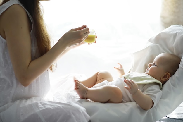 Notion de maternité. Une jeune mère nourrit son petit bébé. Premier leurre et allaitement. Grande famille en vêtements blancs.