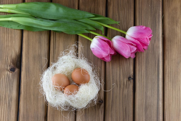 Notion de Pâques. Vue de dessus des tulipes roses et des oeufs de Pâques dans le nid sur fond de bois